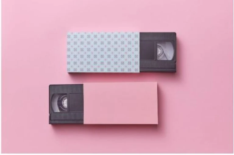 Two VHS tapes in a pink and blue designed cover are placed on a pink background.