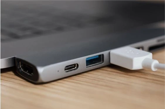Closeup image of  a USB inserted into a laptop placed on a wooden table.