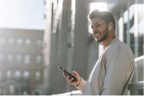 Image of a happy man listening to music using AirPods and a mobile phone on the street.