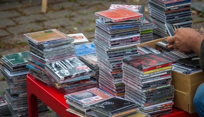 An image of a vendor selling CDs and DVDs piles up on the red table.